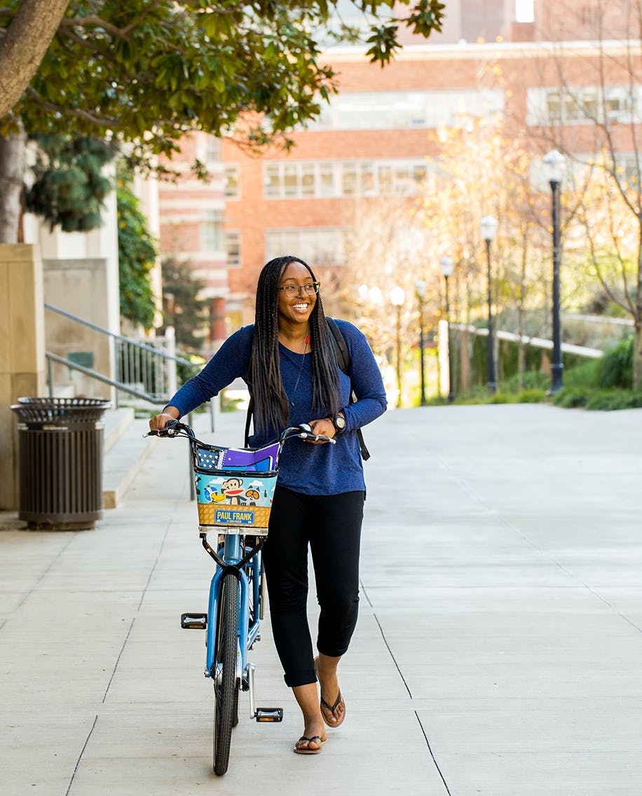 student walking alongside her bike on campus
