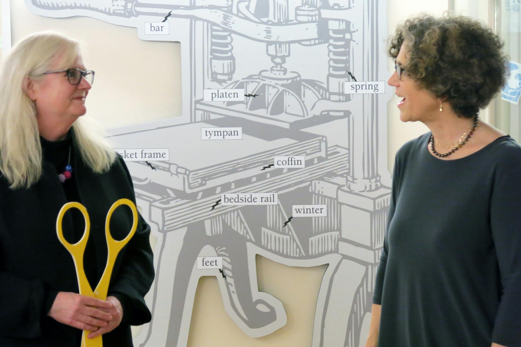 UCLA Librarian Virginia Steele (at left) and IS Professor Johanna Drucker prepare to cut the ribbon on the exhibit of an antique printing press in Powell Library.