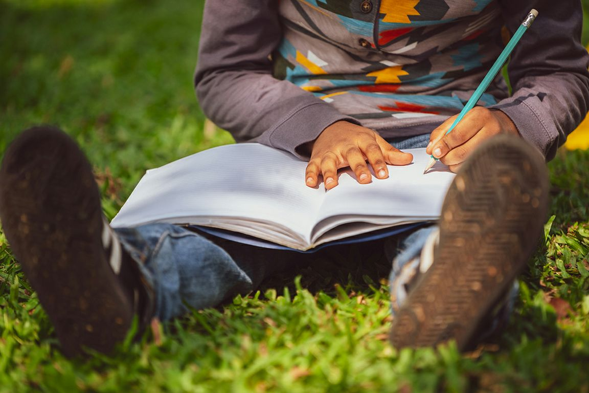 Child sitting on grass writing in notebook
